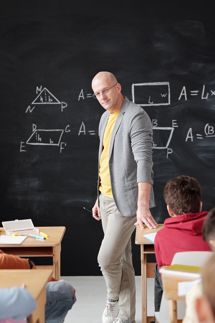 Teacher explaining mathematical concepts on blackboard in a classroom setting.