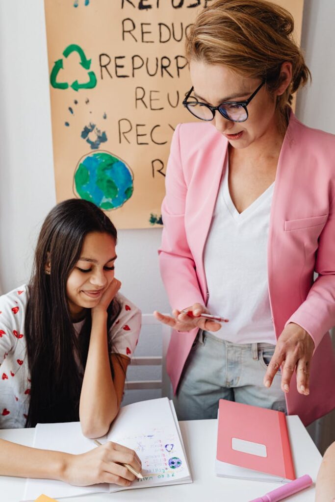 Female teacher assisting teenage girl with homework in classroom setting.